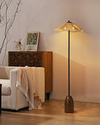 A Clérachic floor lamp with a raffia shade beside a carved wooden cabinet and a cream armchair draped with a fringed throw.