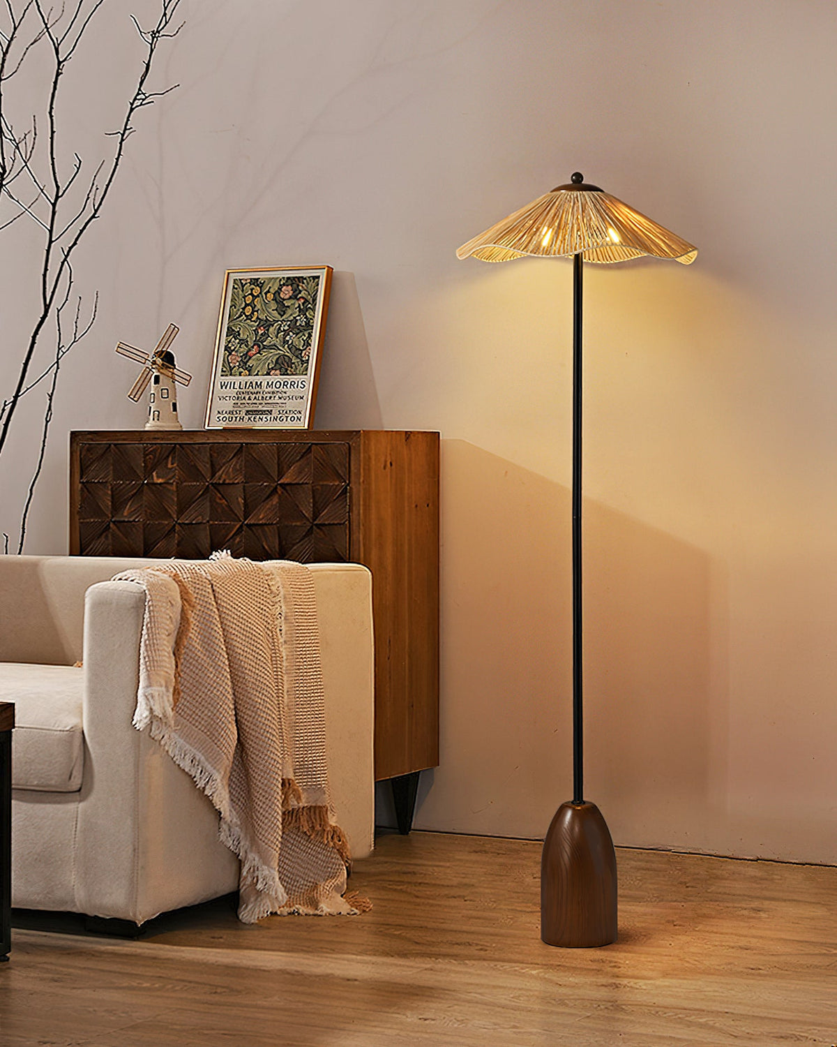 A Clérachic floor lamp with a raffia shade beside a carved wooden cabinet and a cream armchair draped with a fringed throw.