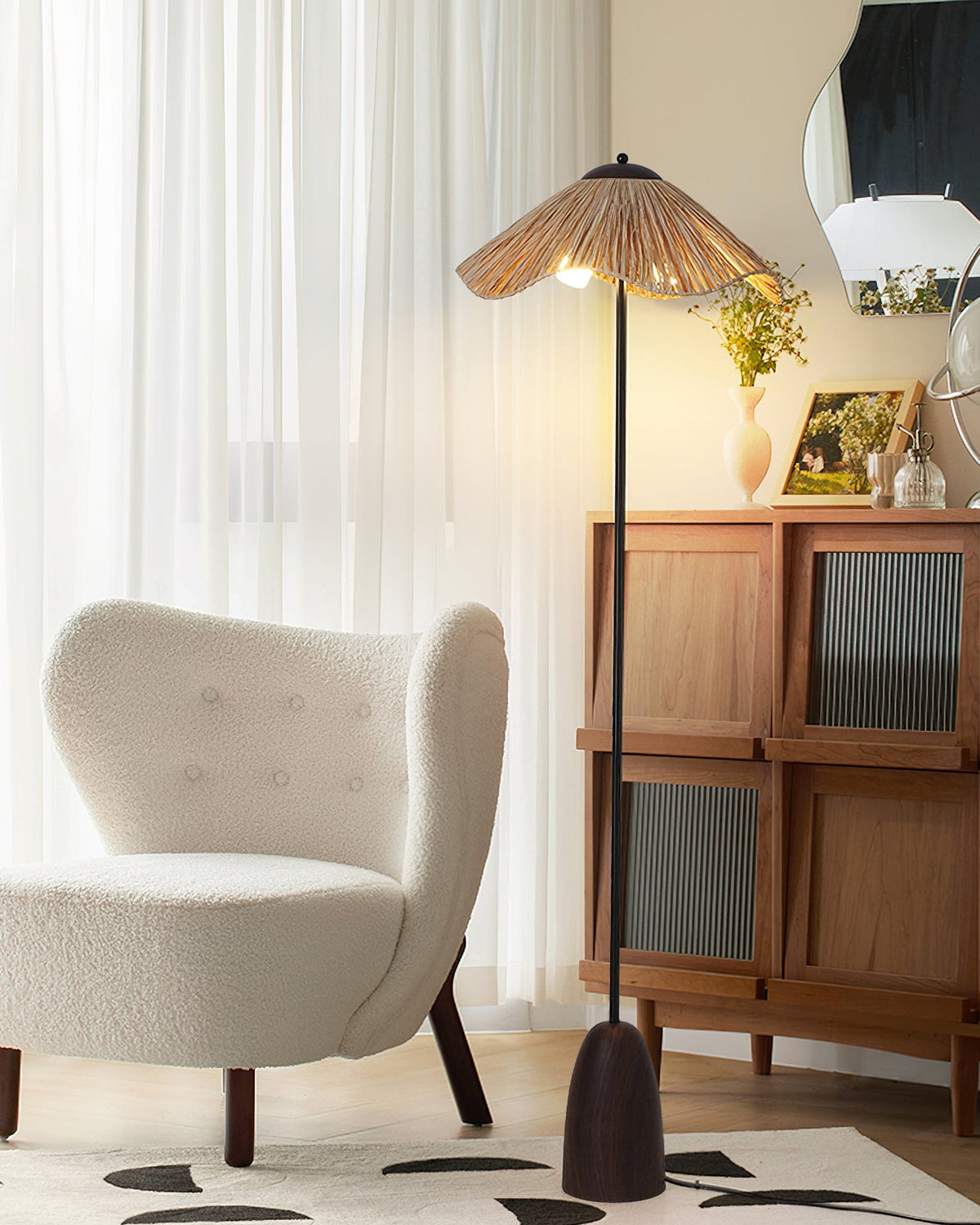 A Clérachic floor lamp with a raffia shade stands beside a white boucle armchair and a wooden cabinet with ribbed glass doors.