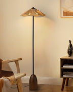 The Clérachic floor lamp's raffia shade glows warm above a rattan armchair and a small wooden shelf, with a figurine nearby.