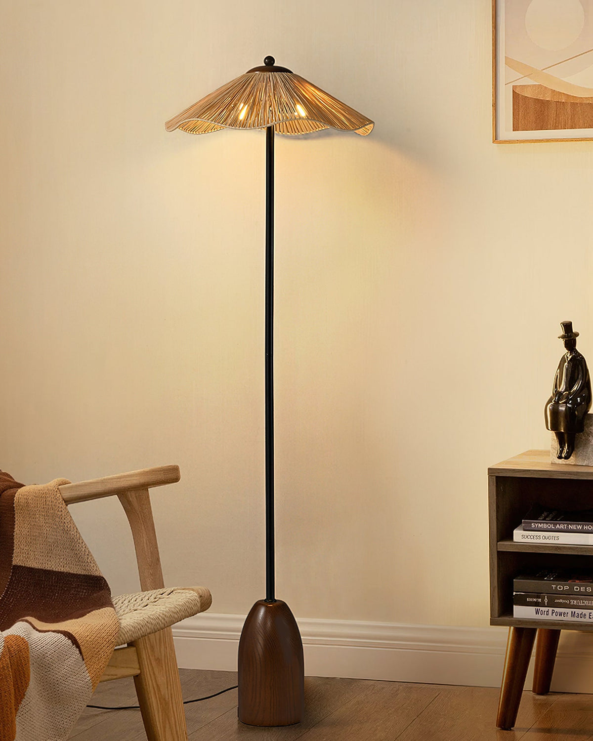 The Clérachic floor lamp's raffia shade glows warm above a rattan armchair and a small wooden shelf, with a figurine nearby.