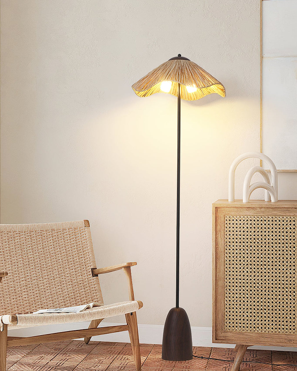 A Clérachic raffia floor lamp lit in a light room with a woven chair and a cane-fronted cabinet.