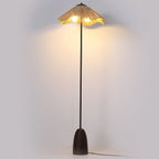 Lit Clérachic floor lamp on a pale grey backdrop, its raffia shade glowing and a soft pool of light on the wall behind.