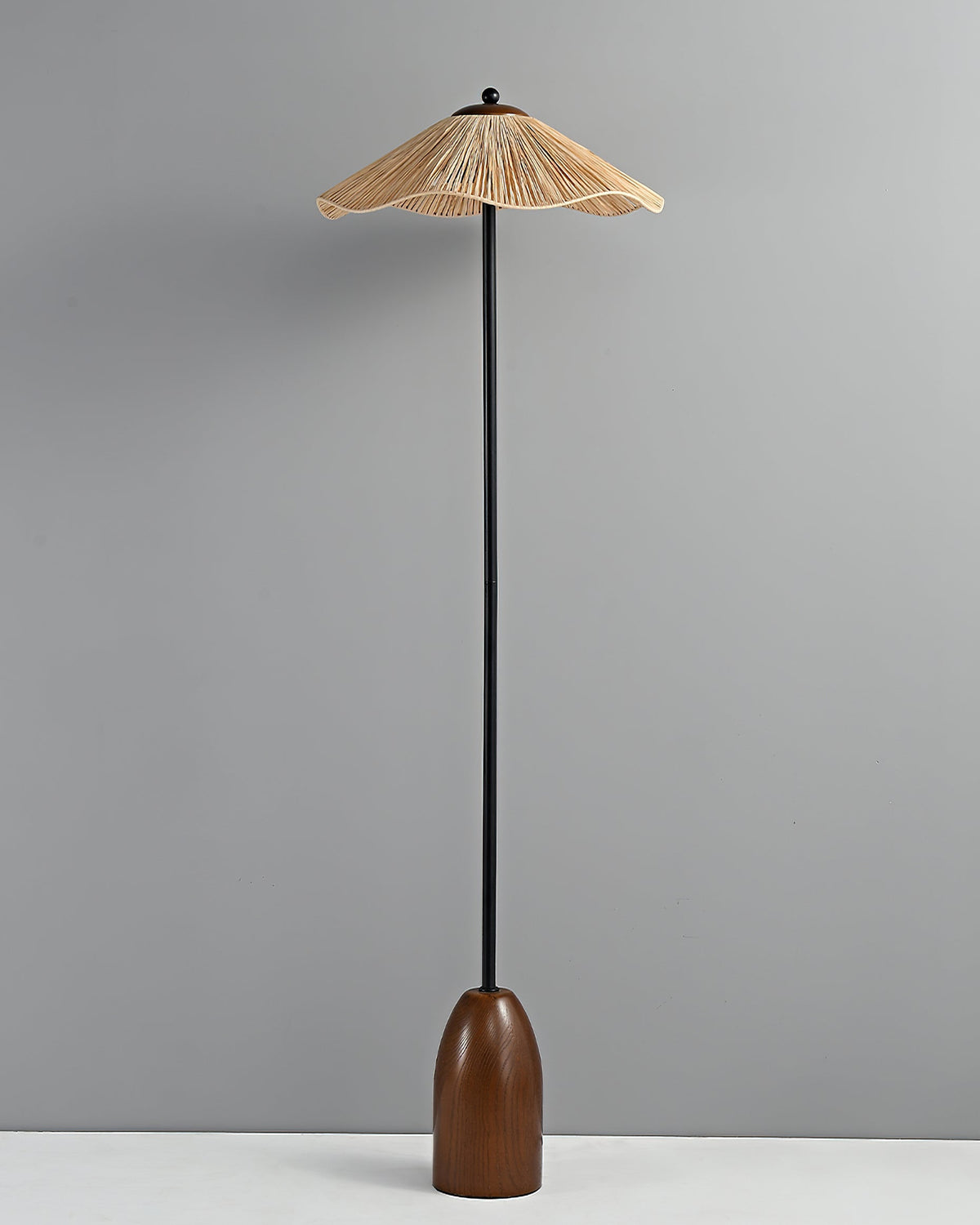 The Clérachic floor lamp with its raffia shade unlit, standing on a pale floor against a grey wall.