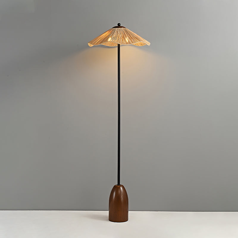 Clérachic floor lamp in the dark walnut finish, its raffia shade lit and casting a soft glow on the grey wall behind.