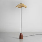 Full view of the Clérachic raffia-shade floor lamp on a grey floor, with its black cord and foot switch trailing off to the right.