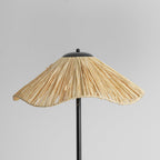Close view of the wavy raffia shade of this Clérachic floor lamp, with the black cap on top and the stem below.