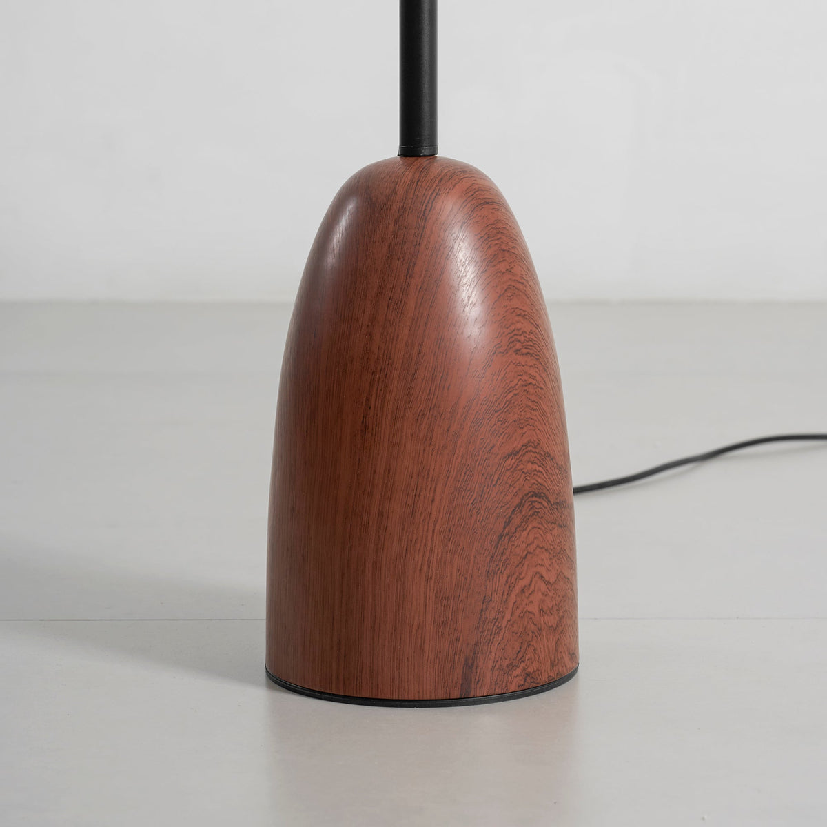 Close view of the rounded walnut base of this Clérachic floor lamp, showing its wood grain and the black stem rising from it.