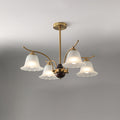 Clérachic Flora chandelier with four fluted glass bell shades on curved brass arms, lit on grey.