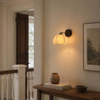 Clérachic wall light glowing beside a framed landscape at a staircase landing, above a small wooden console with a clay pot.