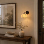 Clérachic wall light with a warm glow above a dark wood console with a bowl, a vase of dried branches and a framed print.