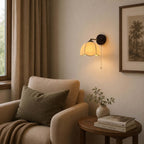 Clérachic wall light with a pull chain above a cream armchair and a round side table, by a window with linen curtains.