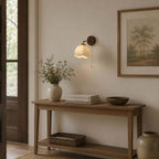 Clérachic wall light above a slim wooden console with a woven basket, a bowl and a framed tree print on the wall.