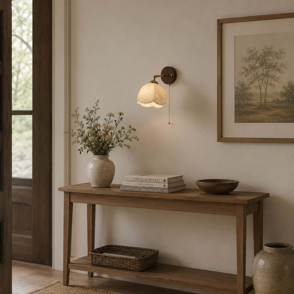 Clérachic wall light above a slim wooden console with a woven basket, a bowl and a framed tree print on the wall.