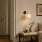 Clérachic wall light with a patterned fabric shade above a cushioned stool, a vase of dried stems and a bedroom door.
