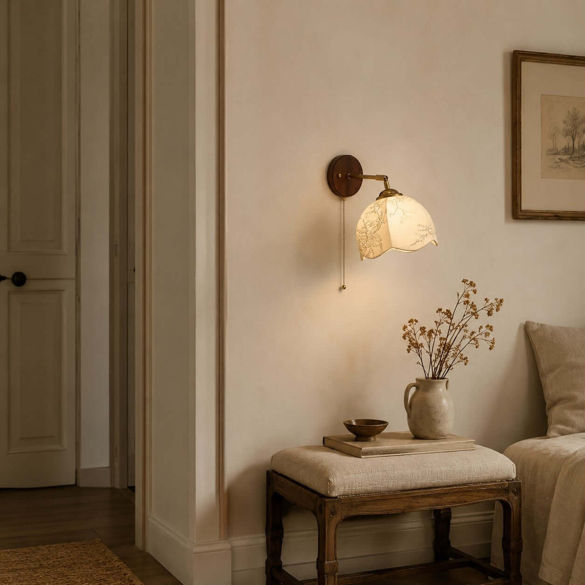 Clérachic wall light with a patterned fabric shade above a cushioned stool, a vase of dried stems and a bedroom door.