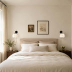 Two Clérachic wall lights with white shades above a linen-dressed bed, either side of a framed print and a small picture.
