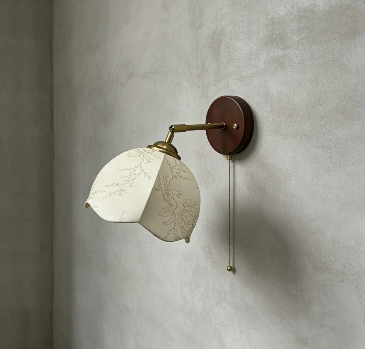 Clérachic wall light with a patterned white shade, a brass arm and a dark walnut-tone plate, on a grey plaster wall.