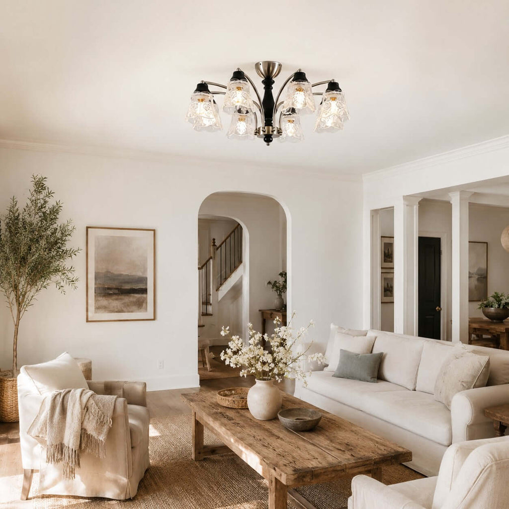 Clérachic nickel and black chandelier with floral glass shades above a rustic wood coffee table, with an arched doorway behind.