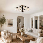 Clérachic nickel and black chandelier with floral glass shades above a rustic wood coffee table, with an arched doorway behind.