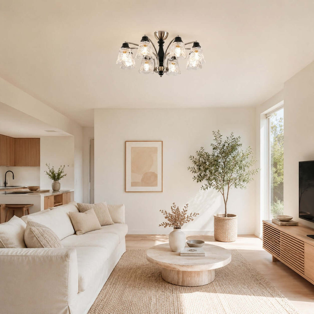 A Clérachic eight-arm ceiling light lit over an open living room, with a round stone coffee table and a tall olive tree.