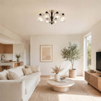 A Clérachic eight-arm ceiling light lit over an open living room, with a round stone coffee table and a tall olive tree.