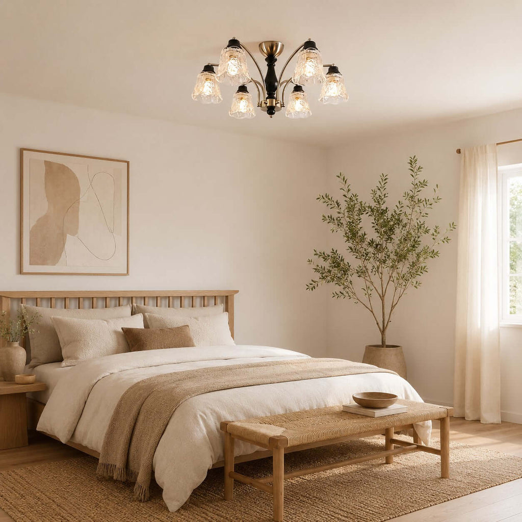 Lit Clérachic chandelier above a bed with a woven headboard and a taupe throw, in a bedroom with a tall olive tree.