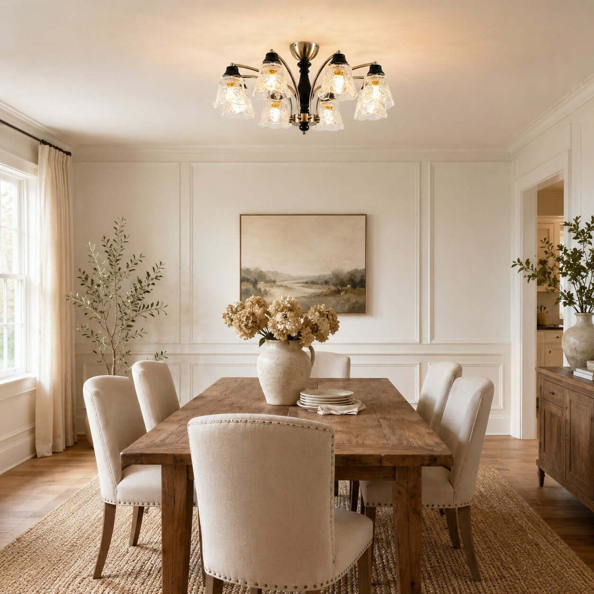 Clérachic nickel-armed chandelier above a rustic dining table with upholstered chairs, a vase of dried flowers and wall panelling.