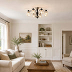 Lit Clérachic chandelier in a living room with built-in white shelves, a green landscape painting and a wood coffee table below.
