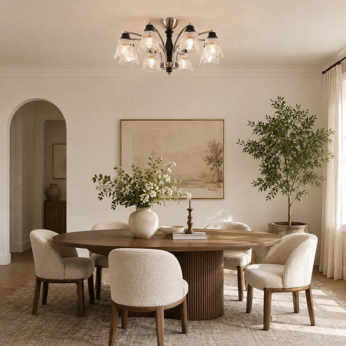 Clérachic glass-shade chandelier above a round wood dining table with boucle chairs, with an arched doorway and a tall plant behind.