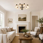 Clérachic chandelier on a white ceiling above a living room with a fireplace, a cream sofa and a rustic wooden table.