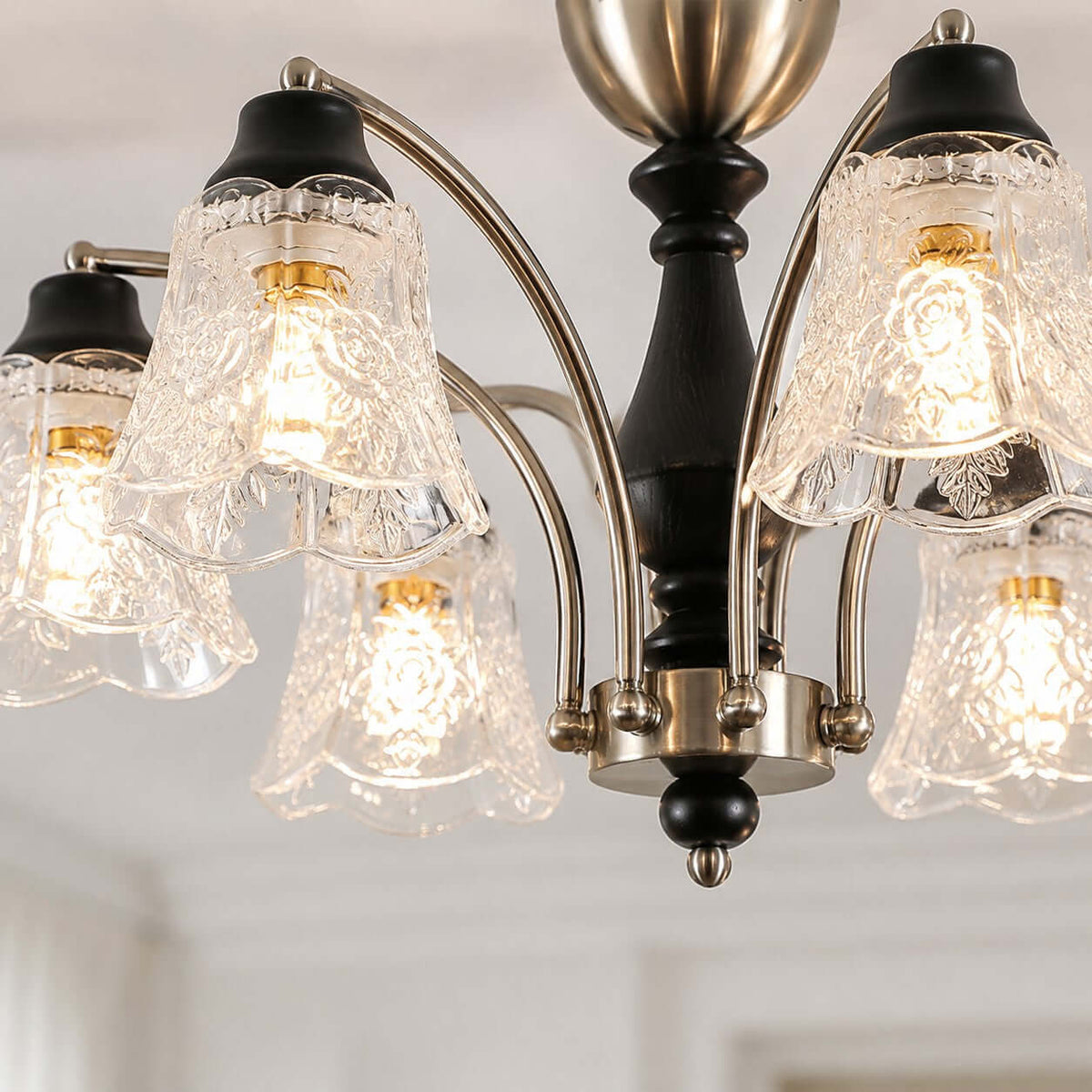 Close view of the floral, rippled clear glass shades, black wooden stem and nickel arms on this Clérachic chandelier.