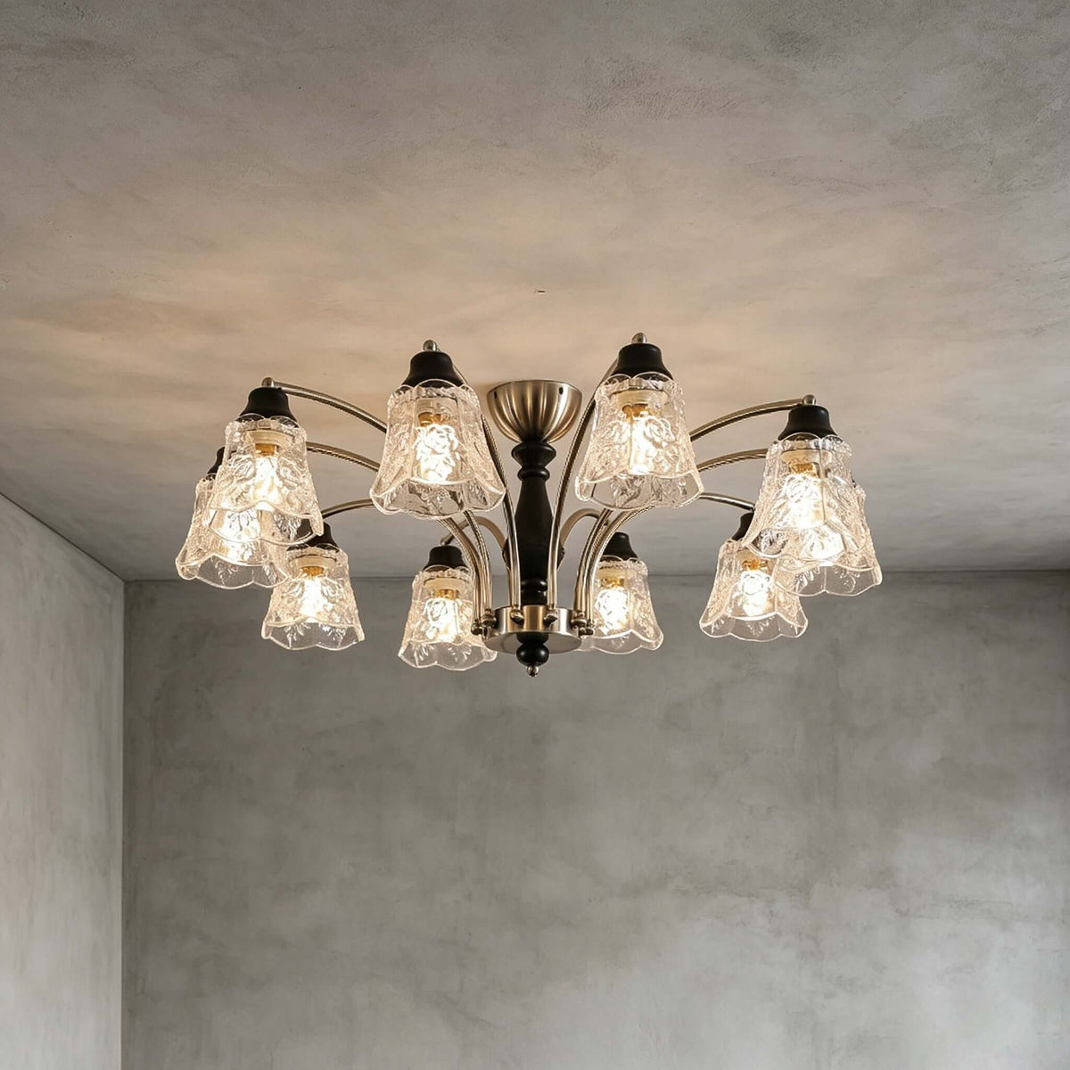 Lit Clérachic ten-light chandelier on a grey concrete-look ceiling, with all its floral glass shades glowing warm.