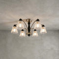 Clérachic six-light chandelier with clear floral glass shades and nickel arms, against a grey plastered ceiling and wall.