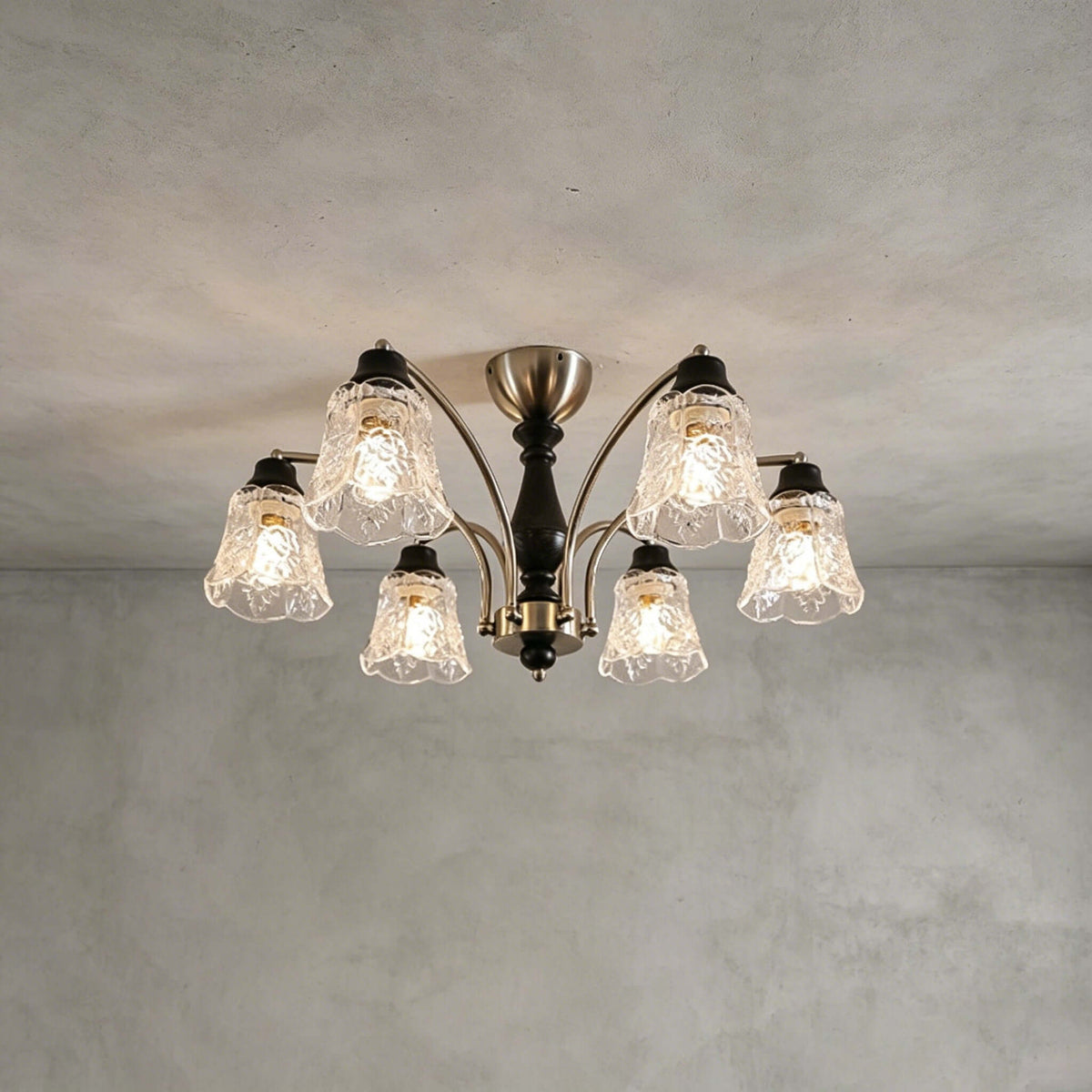 Clérachic six-light chandelier with clear floral glass shades and nickel arms, against a grey plastered ceiling and wall.