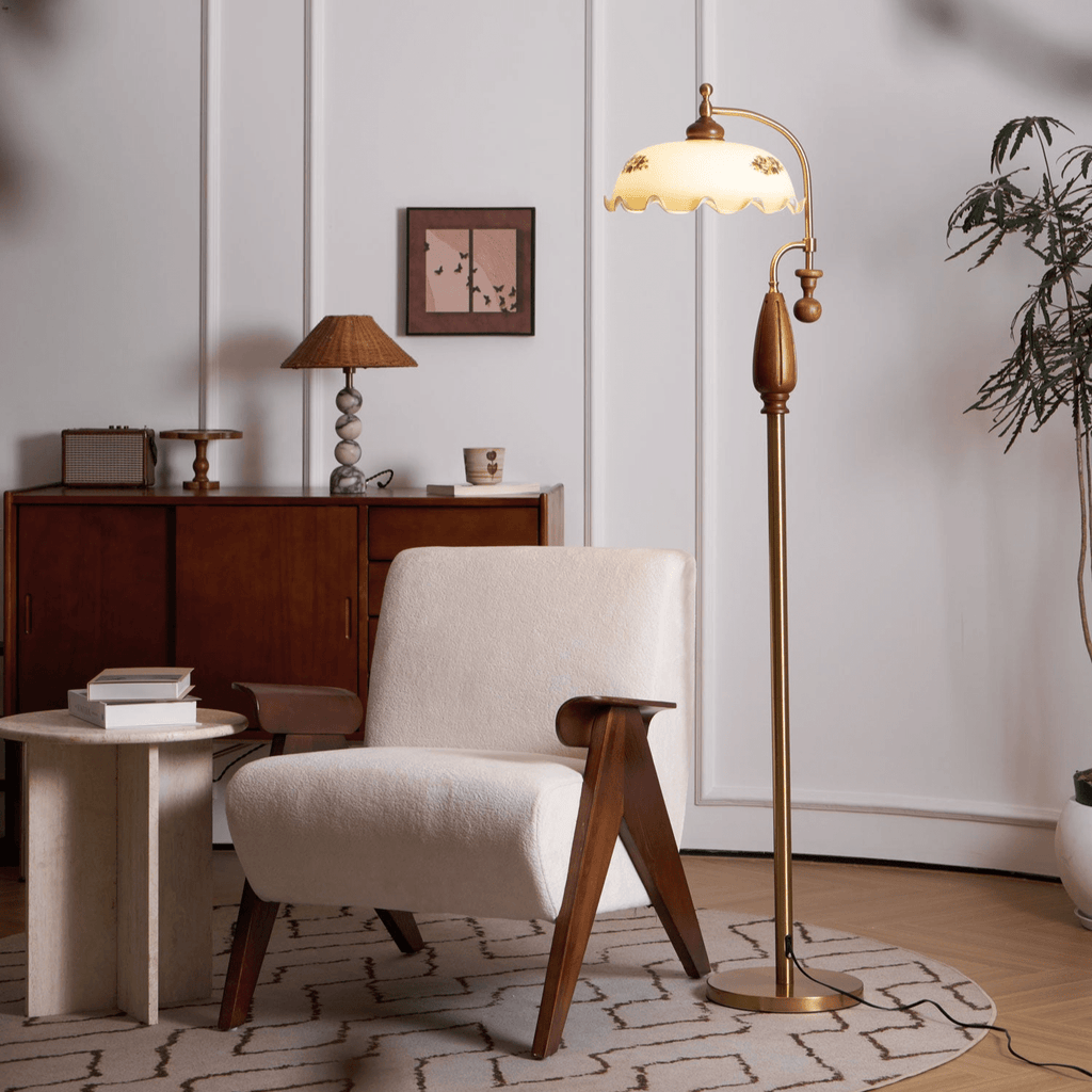 Brass and walnut floor lamp lit beside a cream armchair, with a wooden sideboard and a small woven shade lamp behind; from Clérachic.