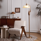Brass and walnut floor lamp lit beside a cream armchair, with a wooden sideboard and a small woven shade lamp behind; from Clérachic.