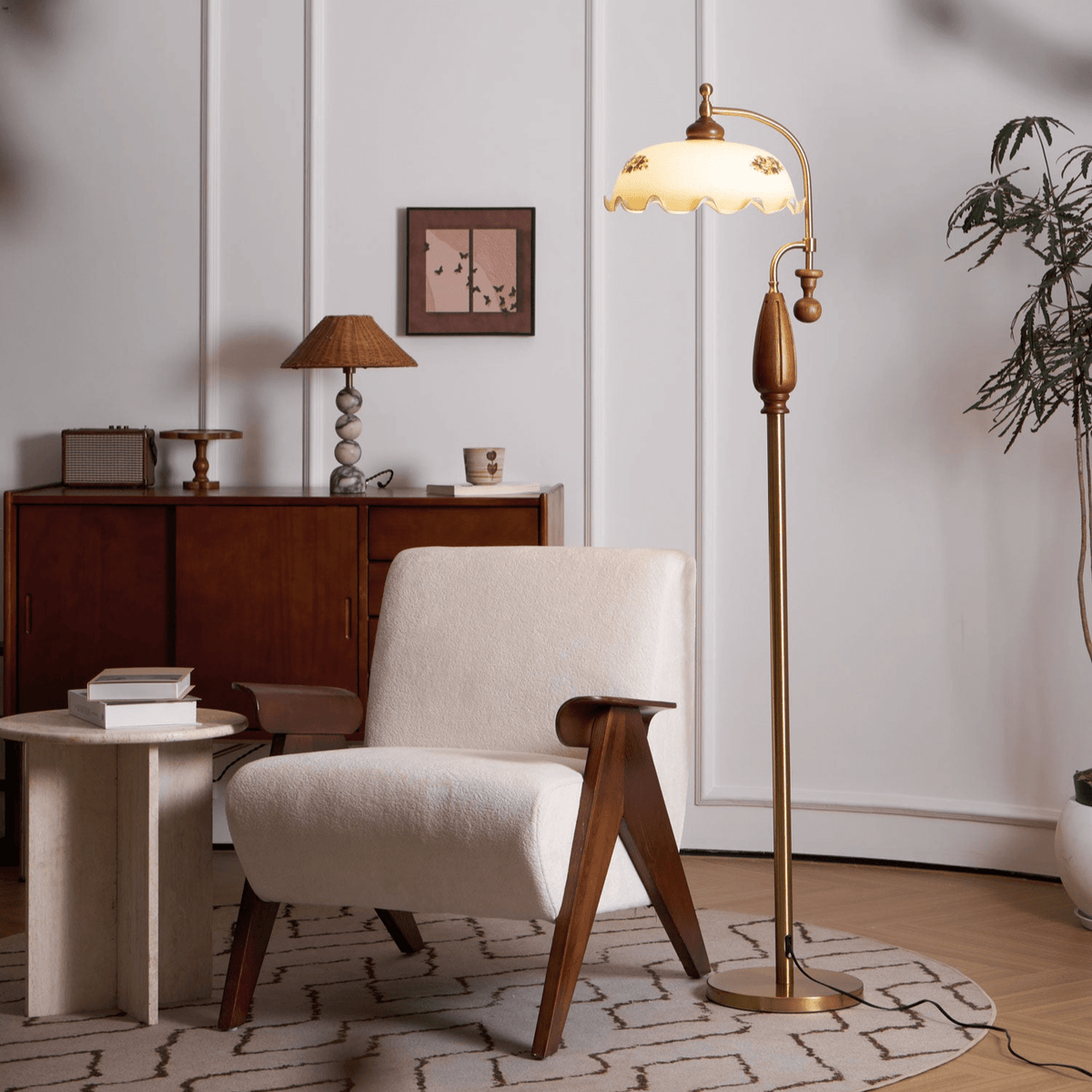 Brass and walnut floor lamp lit beside a cream armchair, with a wooden sideboard and a small woven shade lamp behind; from Clérachic.