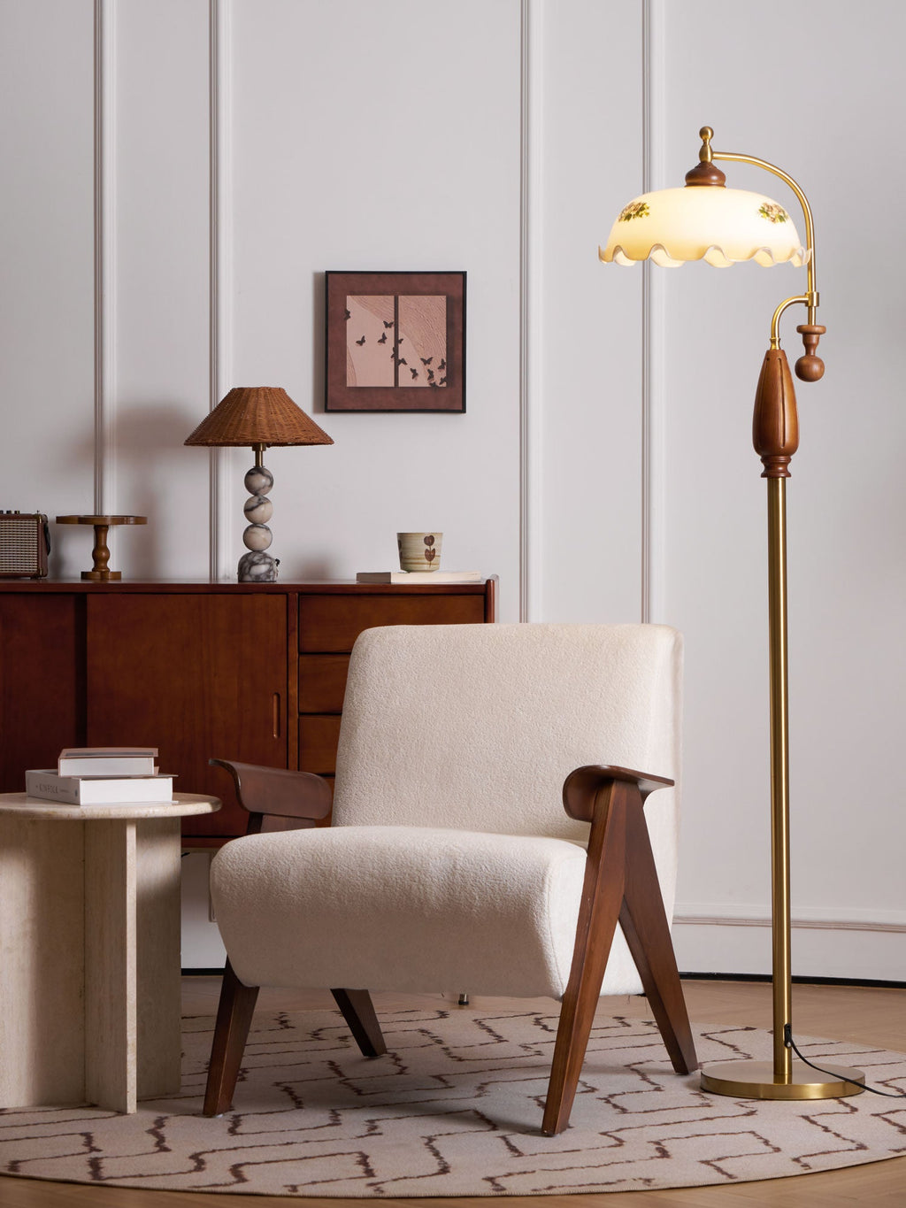 This Clérachic floor lamp stands next to a cream armchair and a stack of books on a travertine table, its shade softly lit.