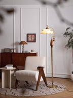 Warm evening scene with the lamp glowing in a corner of panelled white walls, a sideboard and an armchair, with a branch blurred in front; from Clérachic.