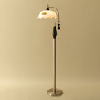 A black-wood and nickel-toned version of the floor lamp on a gold studio backdrop, with the frilled shade lit; from Clérachic.