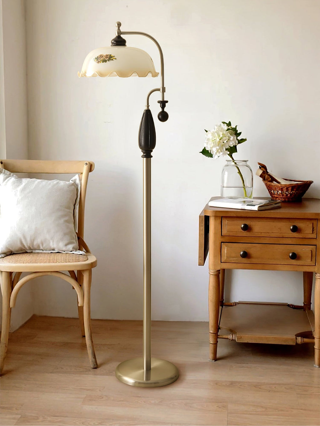 Nickel floor lamp with a black grip stands between a cane chair and a pale wood side table with white flowers; from Clérachic.