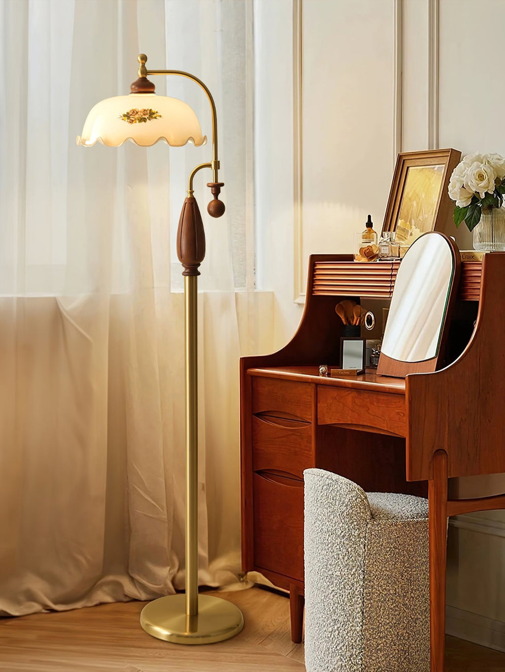Brass floor lamp with a walnut-toned grip glows beside sheer curtains and a wooden dressing table, with a cushioned stool; a Clérachic lamp.