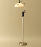 Nickel-toned version with a black wooden grip on a soft gold backdrop, shade lit and frilled; a Clérachic floor lamp.