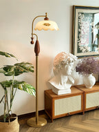Brass floor lamp beside a rattan cabinet that holds a white bust and dried flowers, with a large leafy plant at left; a Clérachic lamp.
