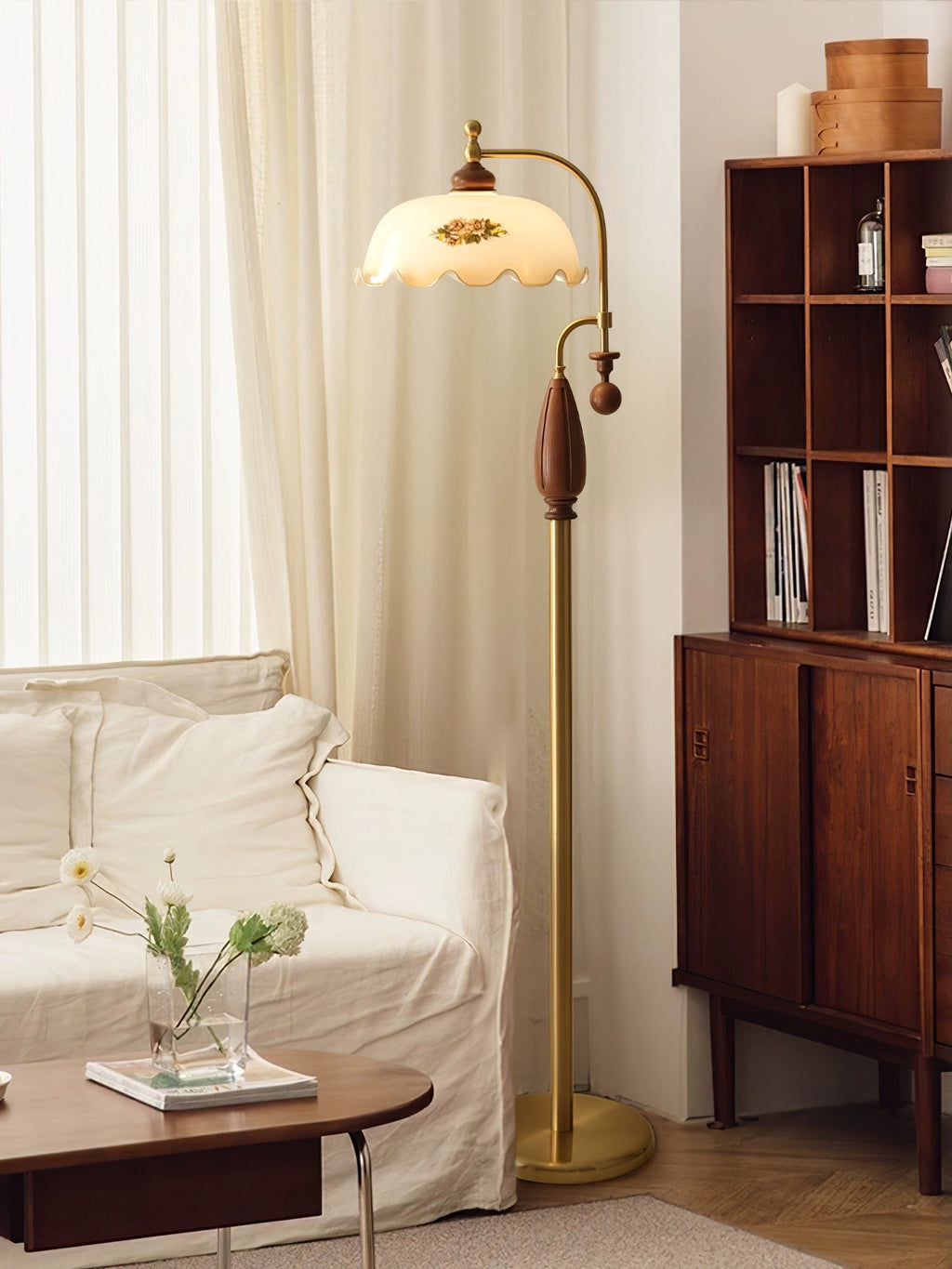 Brass lamp lit in front of cream curtains, next to a white sofa and a wooden bookcase with an oval coffee table; from Clérachic.