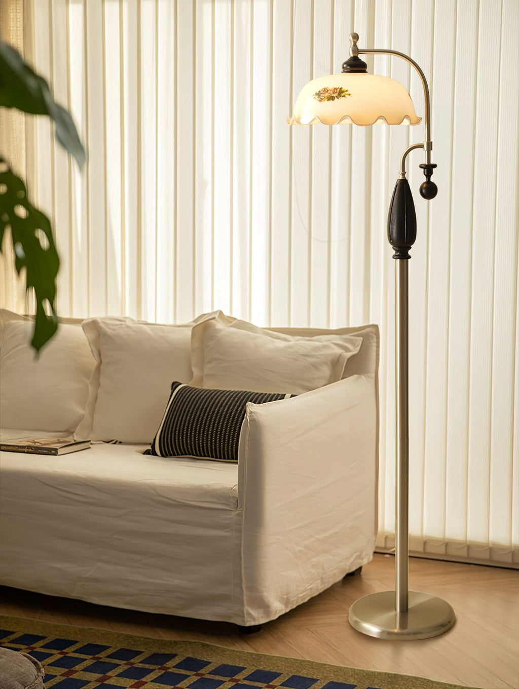 Nickel floor lamp with a black grip stands beside a linen sofa, in front of vertical white blinds; a Clérachic design.