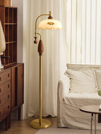 Lit brass lamp between a wooden chest of drawers and a white sofa, with tall cream curtains behind; a Clérachic floor lamp.