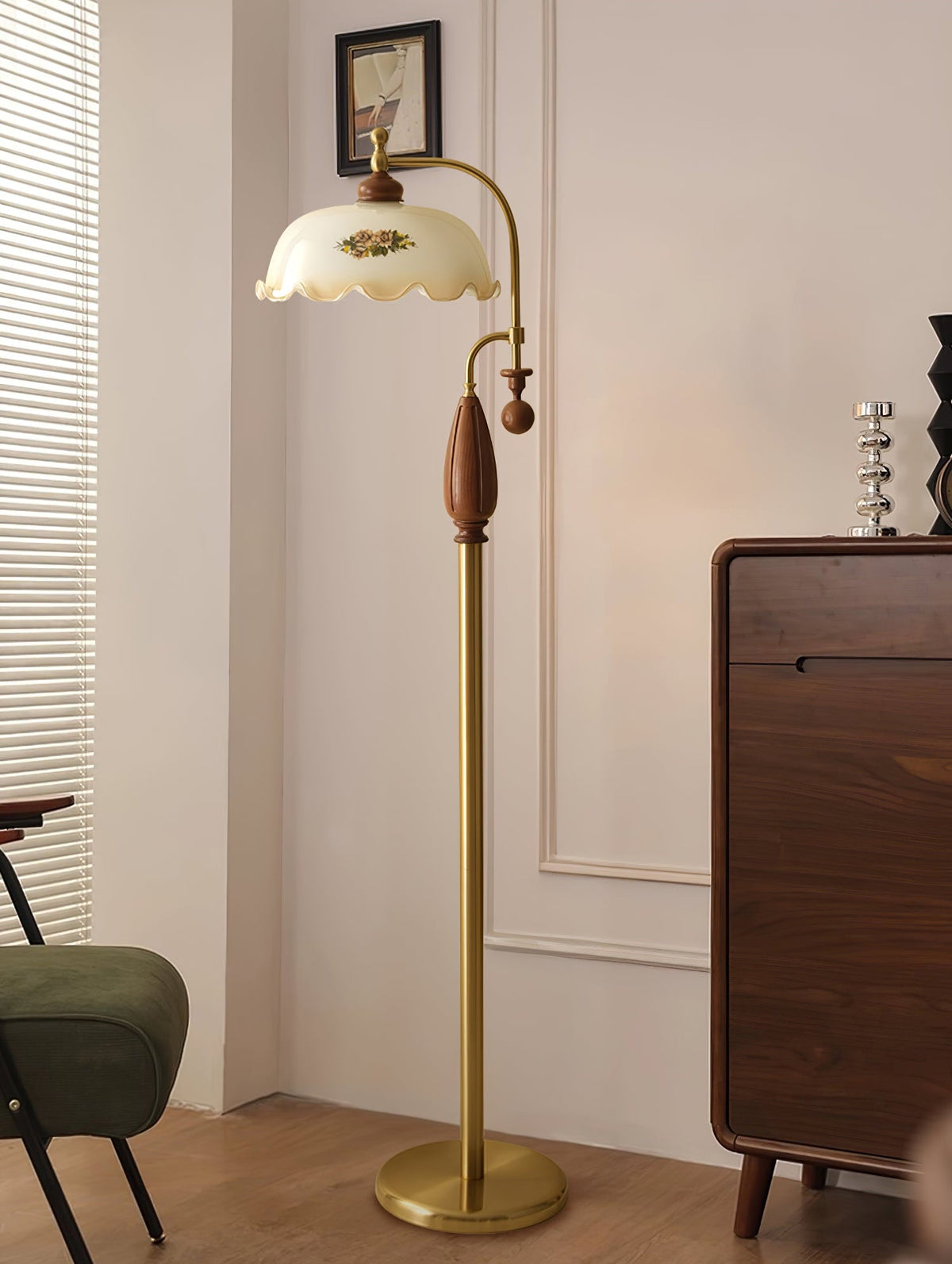 Floor lamp with a frilled shade lit in a pale room, beside a dark wood cabinet, and with a dark-green chair at the edge; from Clérachic.