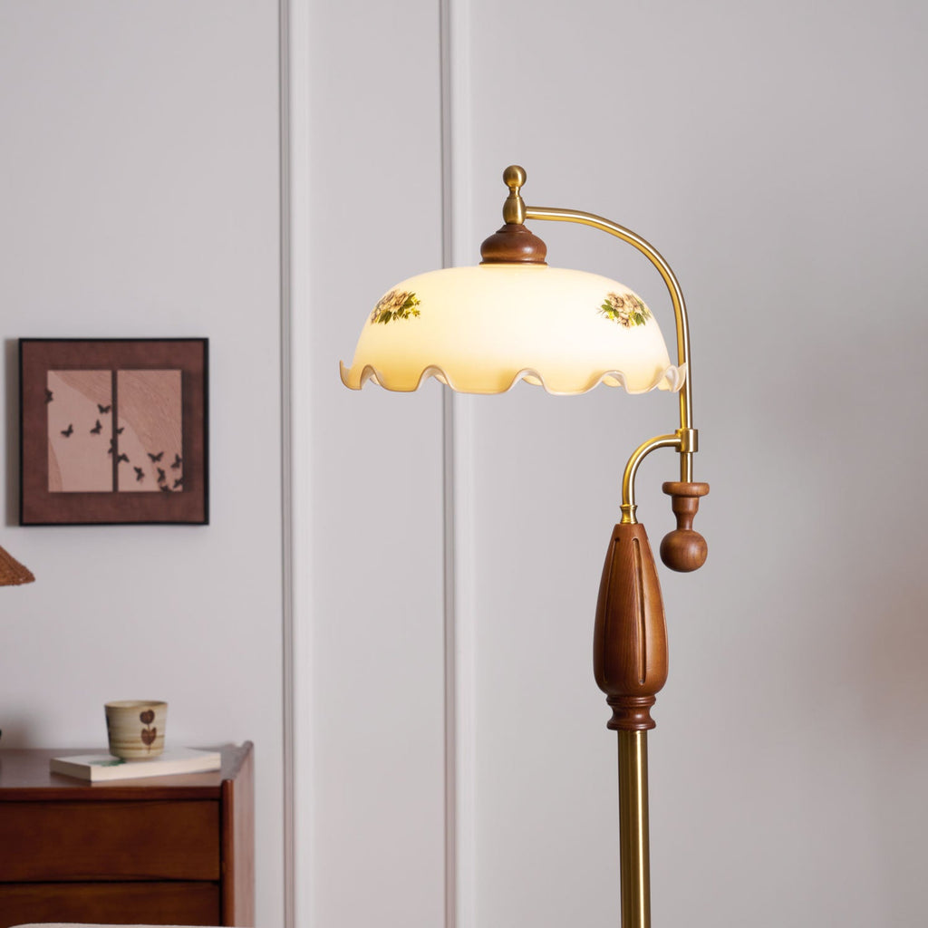 Close view of the frilled floral shade, walnut cap, brass arm and wooden grip, with a framed print behind; a Clérachic floor lamp.